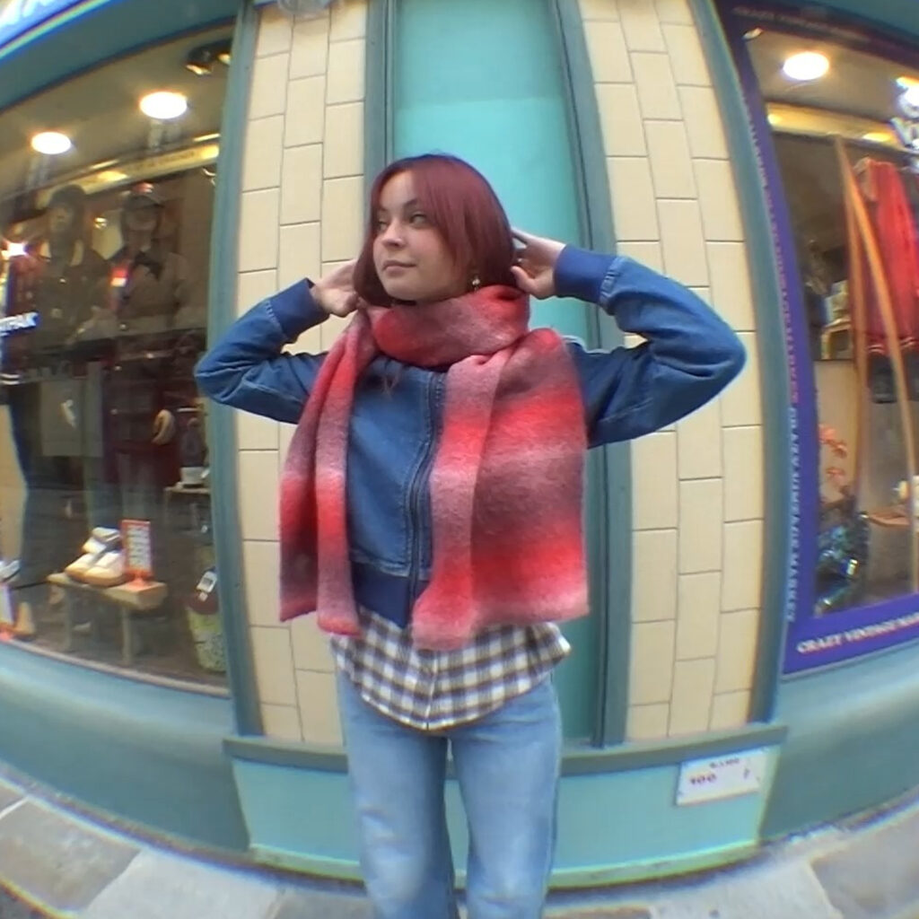 Femme portant un look casual avec veste en jean et écharpe dégradée rouge devant la boutique Kaki Crazy Station.