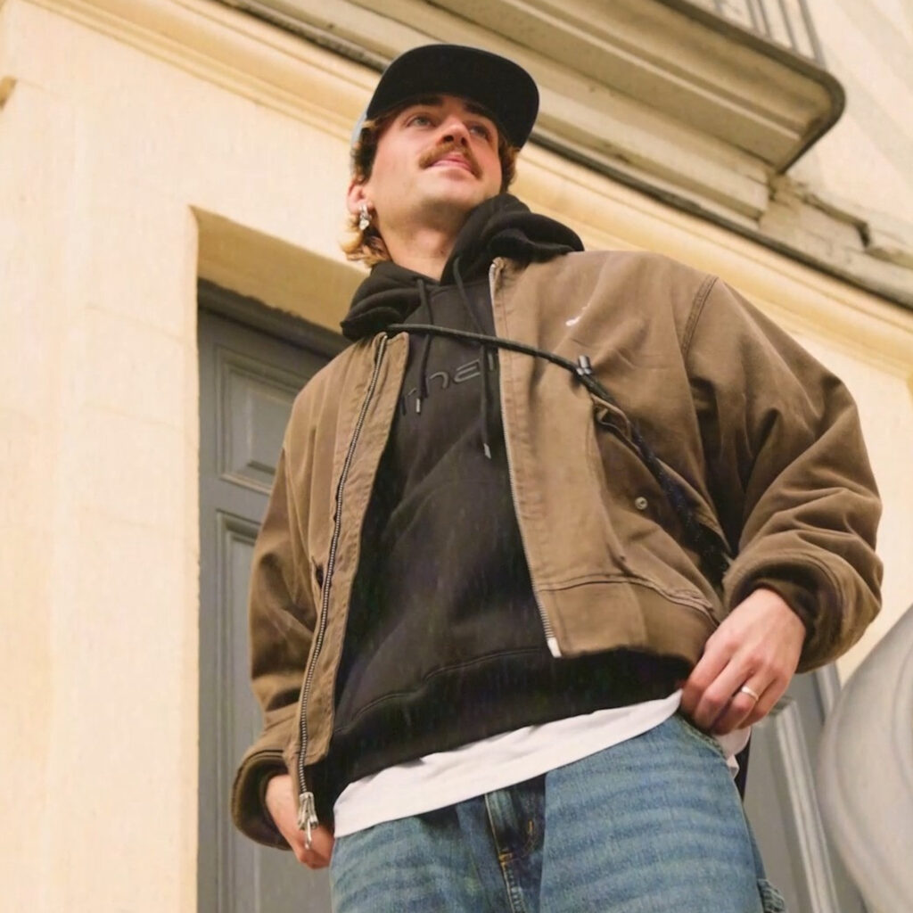 Homme portant un look streetwear avec veste kaki, sweat à capuche noir et jean, style urbain Kaki Crazy Station